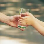 The father gives the child a glass of fresh water. Selective focus. nature.